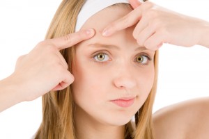 Young woman popping a pimple on her forehead