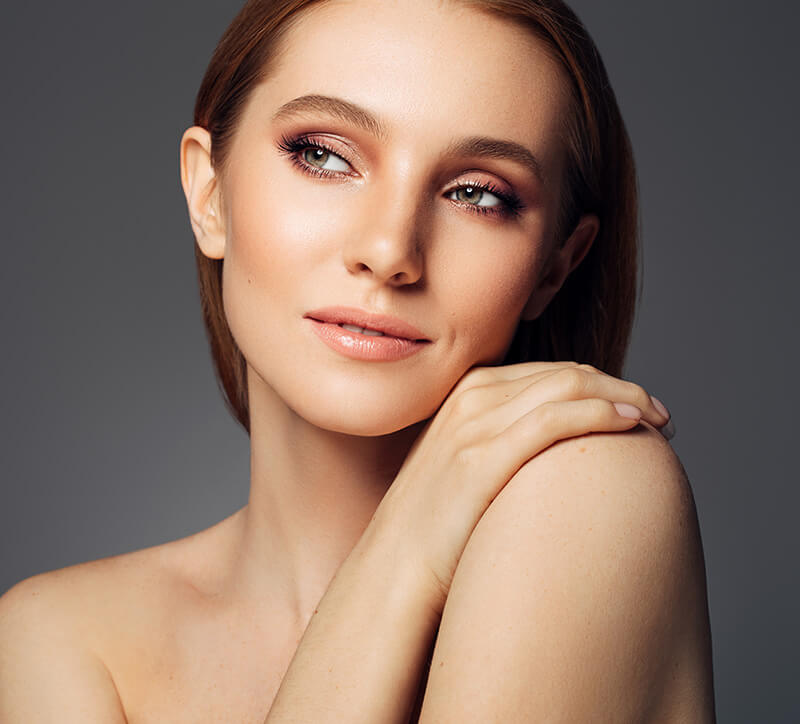 headshot of a woman putting her hand on her bare shoulder