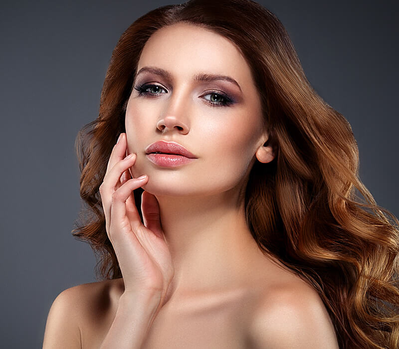 Headshot of a woman putting her hand to her smooth cheek