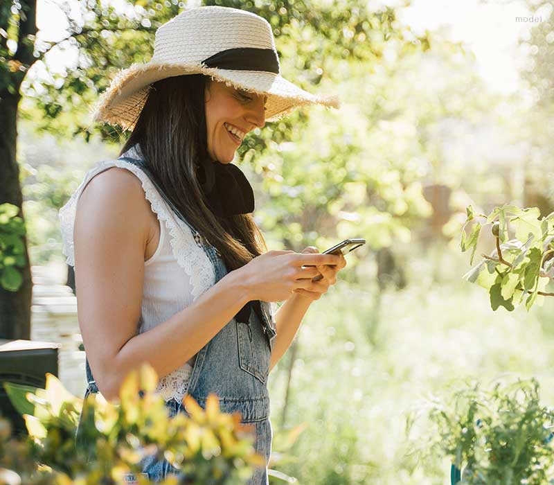 Woman in overalls and a sunhat looking over her plants in a garden - mobile version