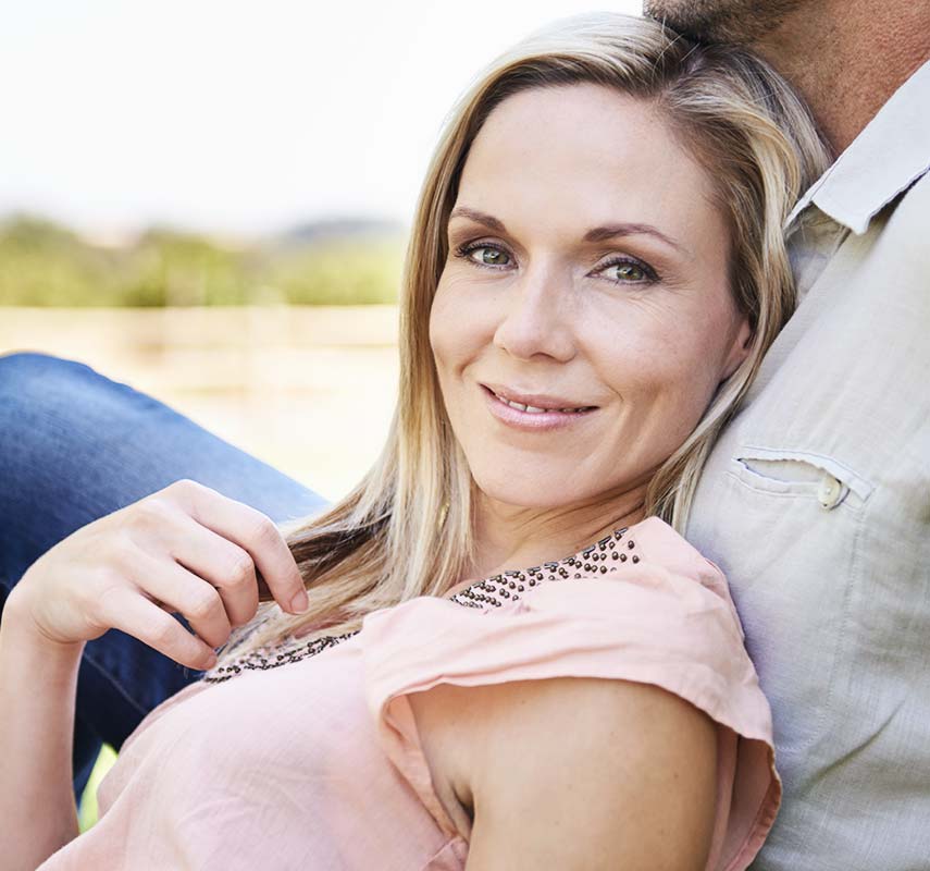 Middle aged female model laying over her husband in a field