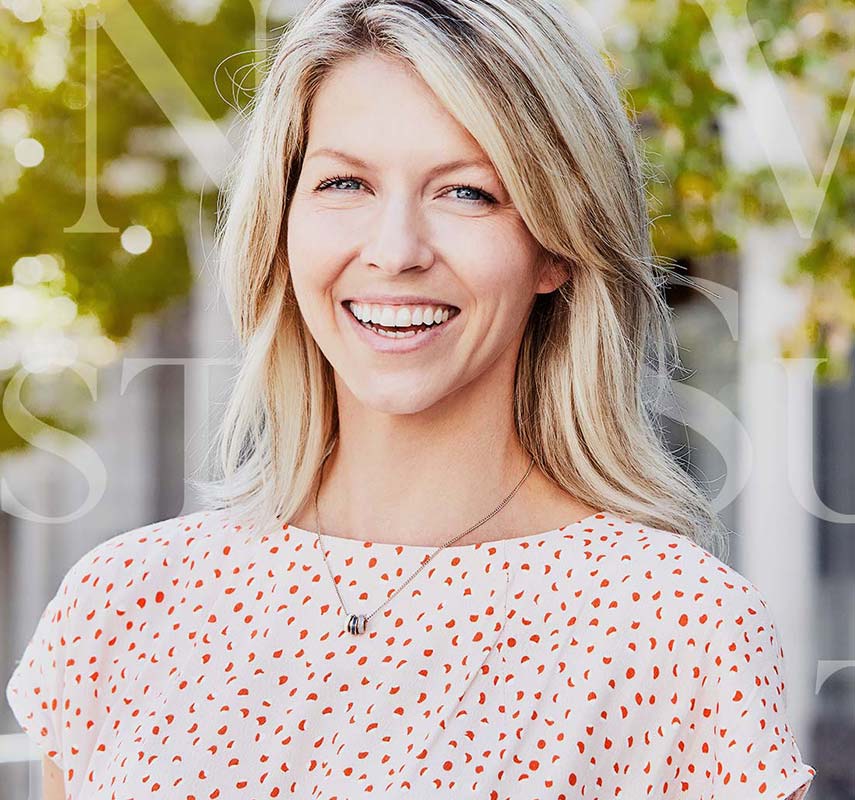 Smiling female model with a house and garden in the background - mobile