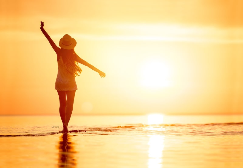 Woman standing on a beach at sunset.